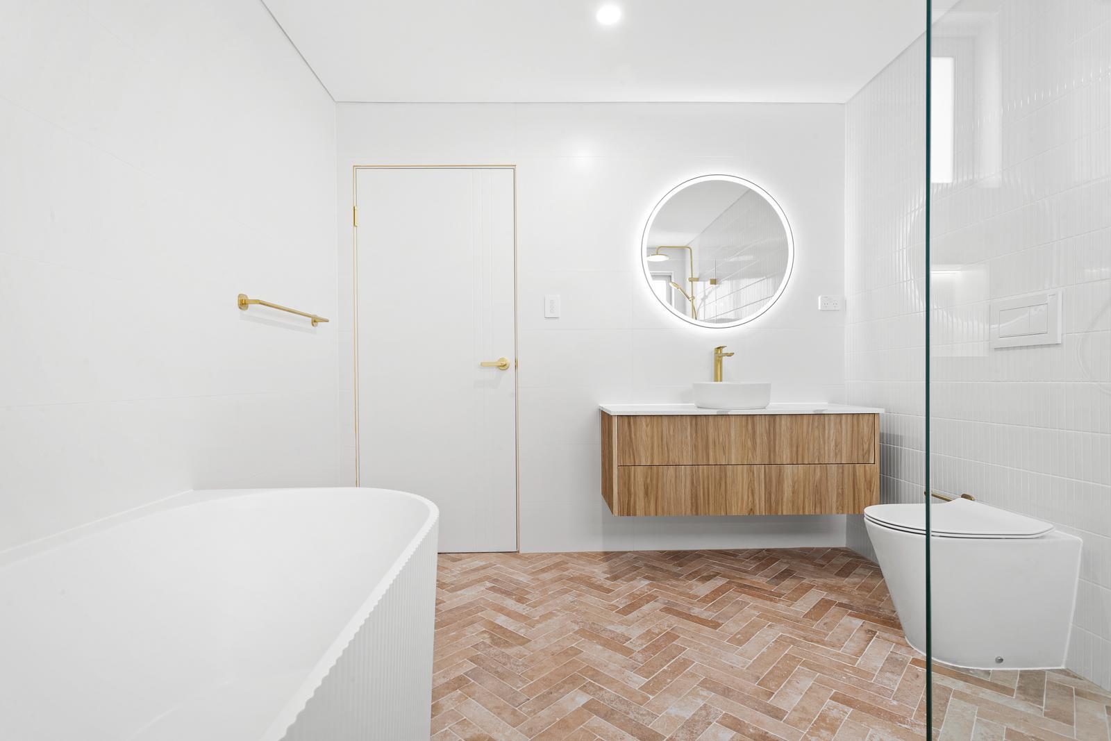 Completed bathroom vanity with round lit mirror, herringbone floor and freestanding bath, Malabar